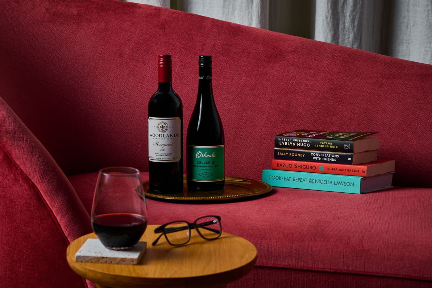 Several books on a couch with a couple of bottles of red wine