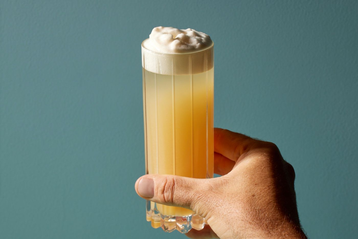 Holding a tall glass of the Aussie Derby Fizz cocktail