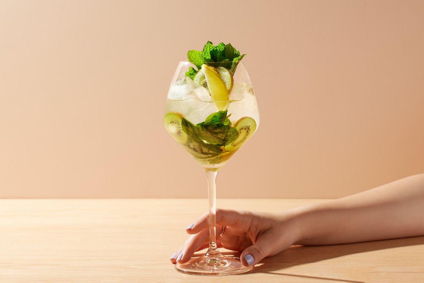 Holding a Pavlova Spritz cocktail, which has fruit and mint as its garnish