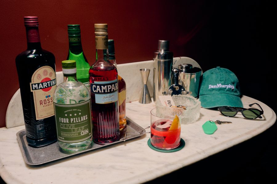 Various spirits bottle on a benchtop with a Negroni and cocktail tools