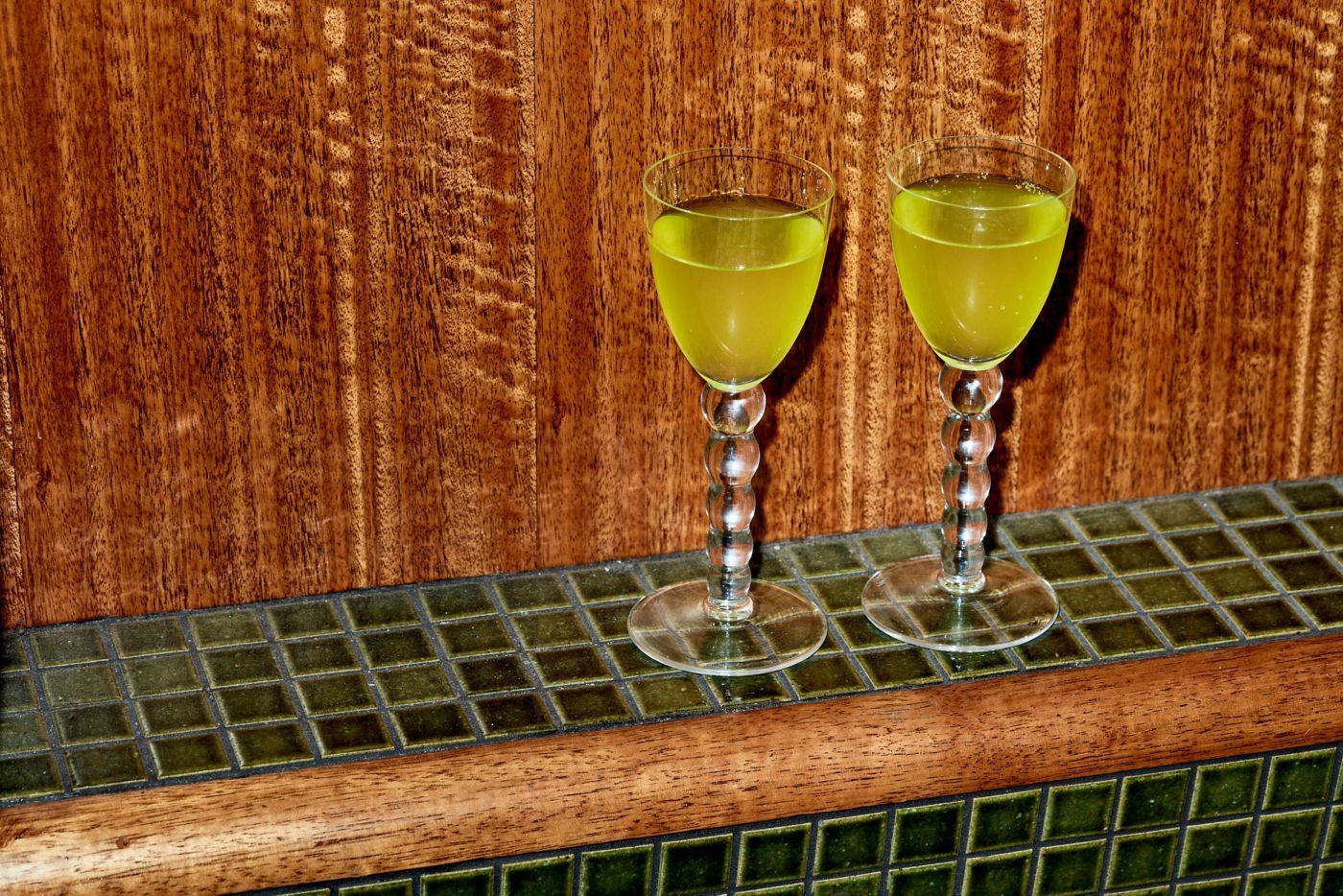 Two glasses of Chartreuse on a green-tiled ledge