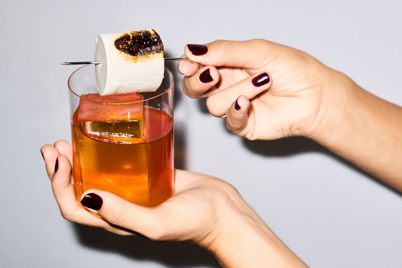 Holding a Toasted Marshmallow Old Fashioned, which has a skewered marshmallow as garnish 