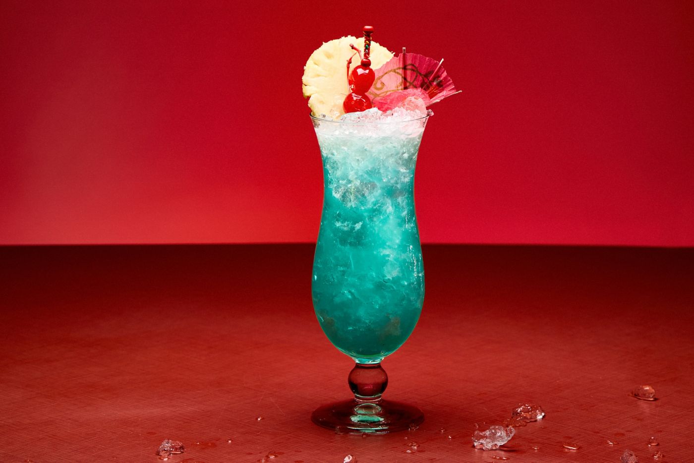 The bright Blue Hawaii cocktail against a deep red background