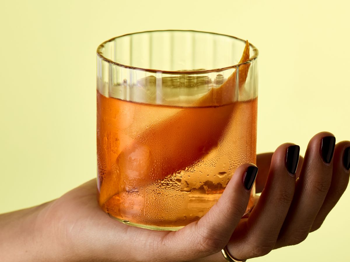 Holding a glass of the mezcal-based Oaxaca Old Fashioned cocktail