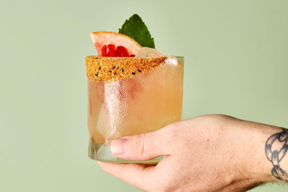 Holding a Tokyo Sour cocktail, garnished with grapefruit, mint and a spice rim