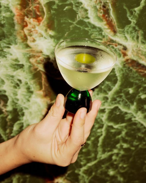 Holding the Tomatini cocktail, which is finished with olive oil on top