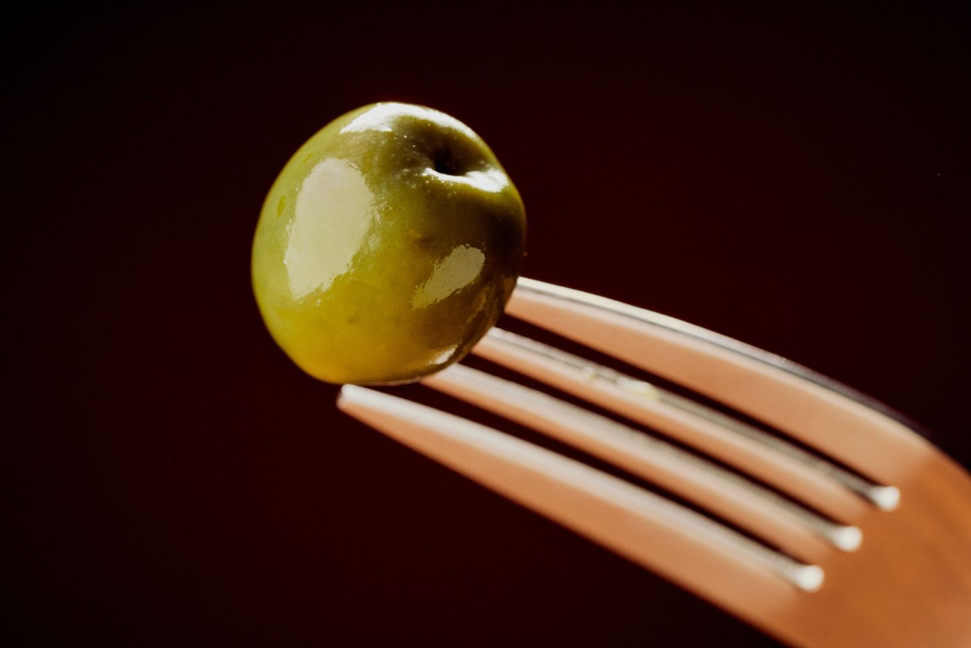 A green olive on a fork against a black background