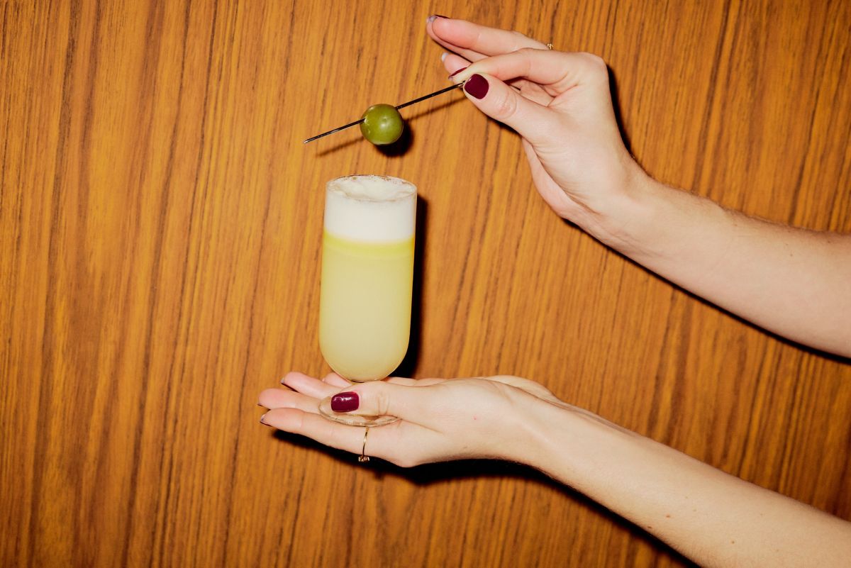 Holding the Oliveto cocktail and a skewered olive as garnish