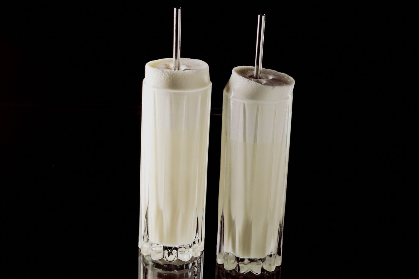 Two hands holding a Ramos Gin Fizz cocktail against a green background