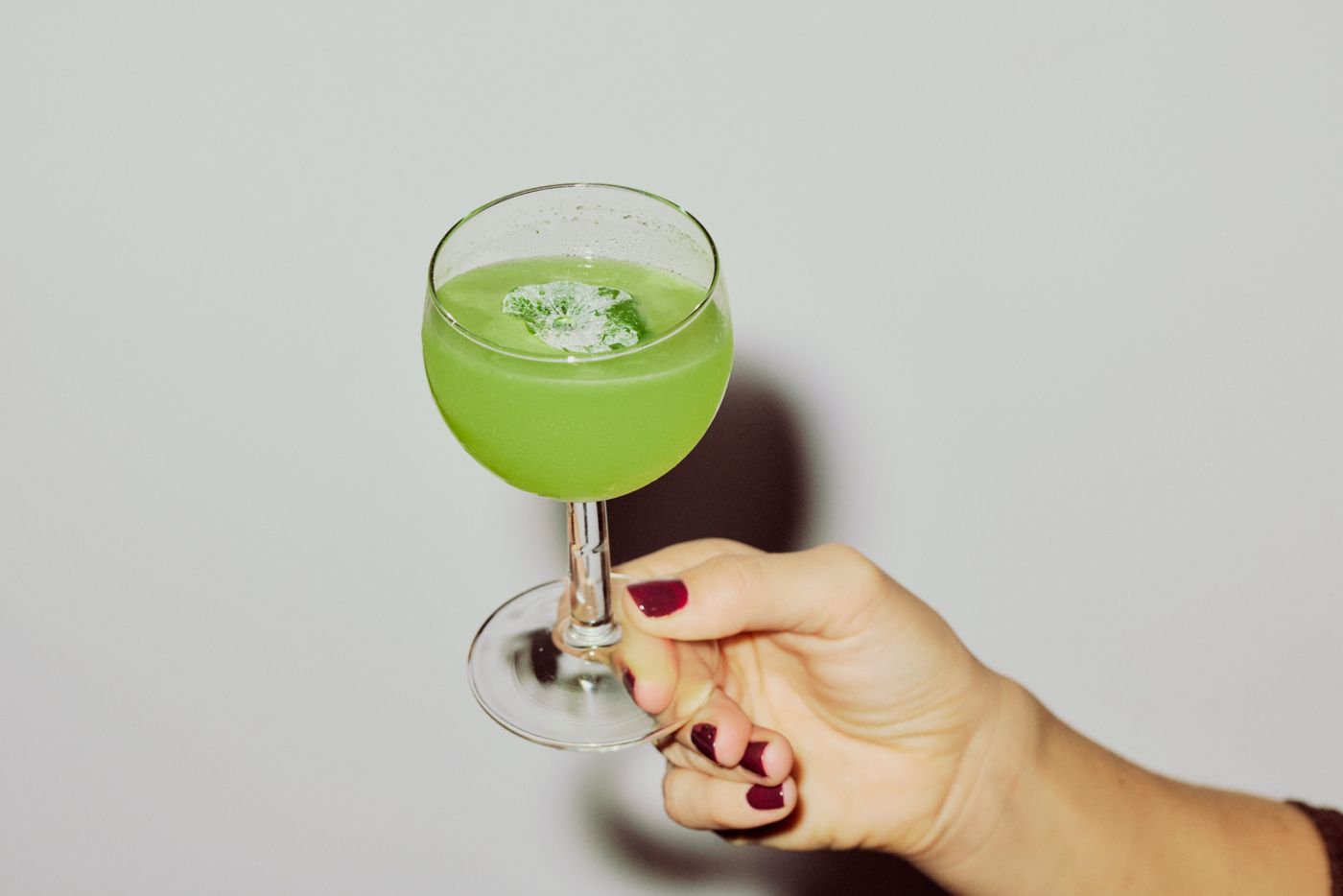 Holding a glass of the peppery, savoury Rocket Gimlet cocktail 
