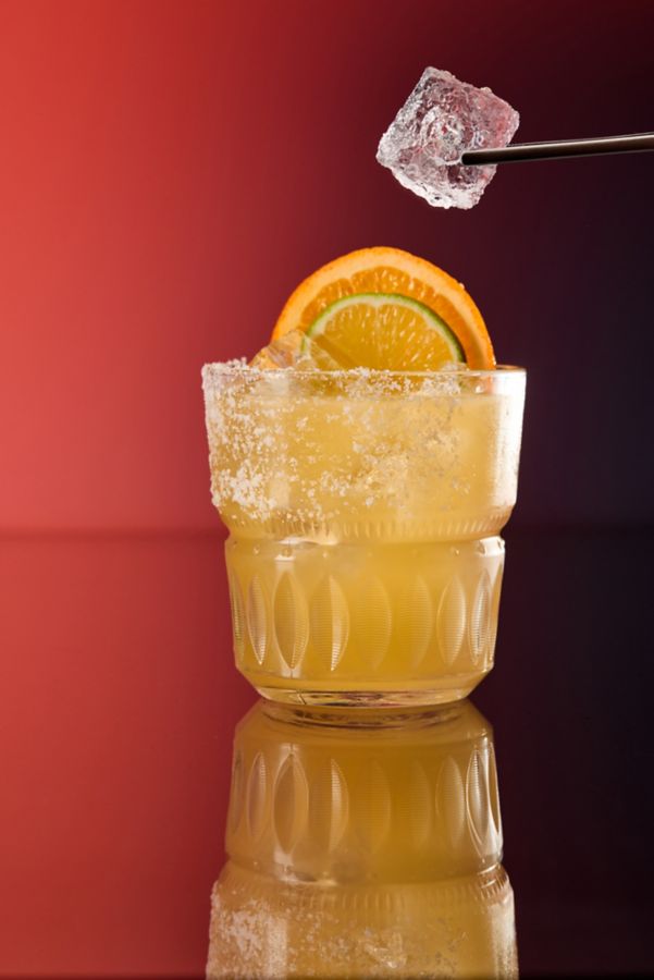 Adding an ice cube to a glass of the Mezcalita cocktail