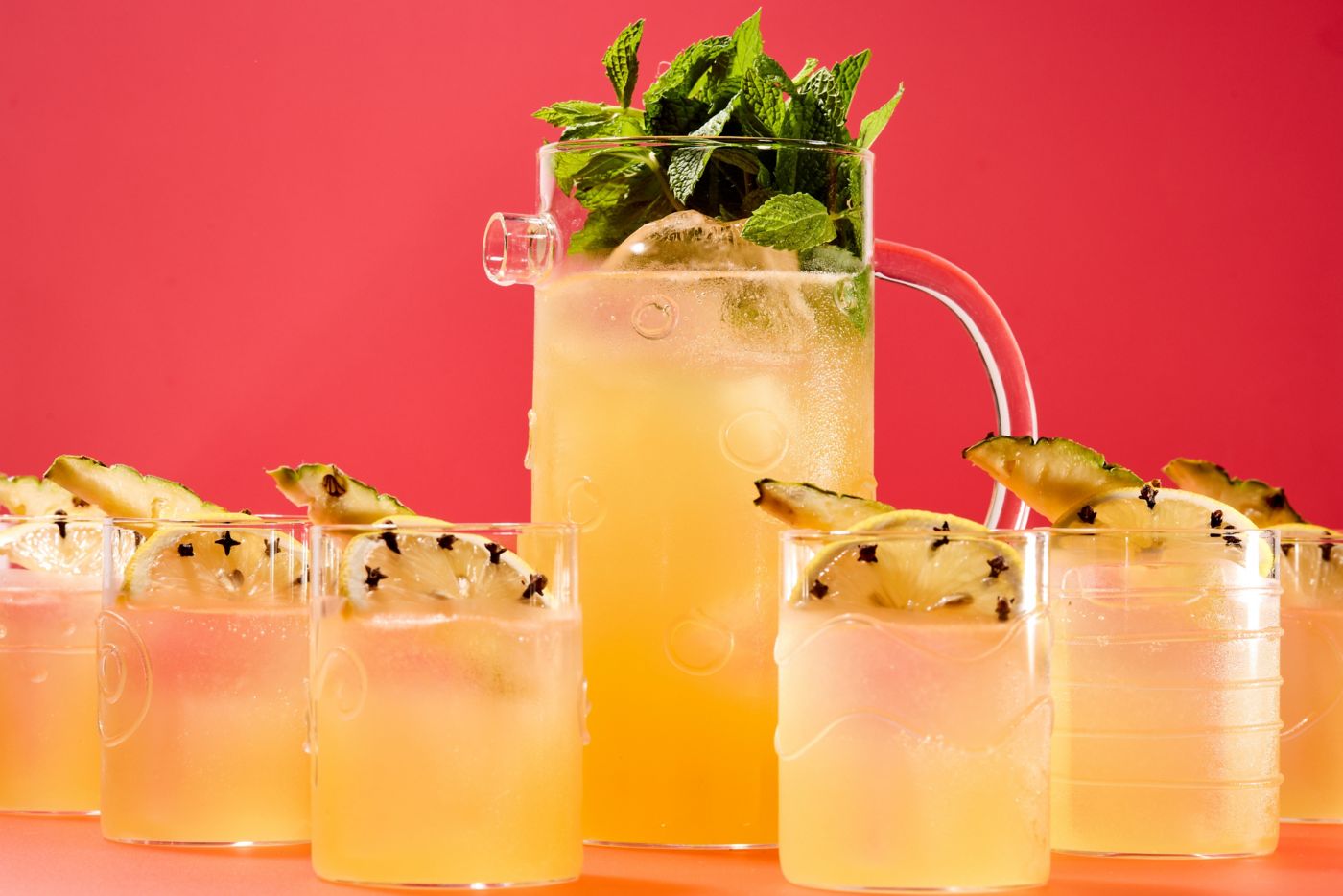 The Pisco Punch cocktail in a jug, with glasses garnished with lemon and pineapple