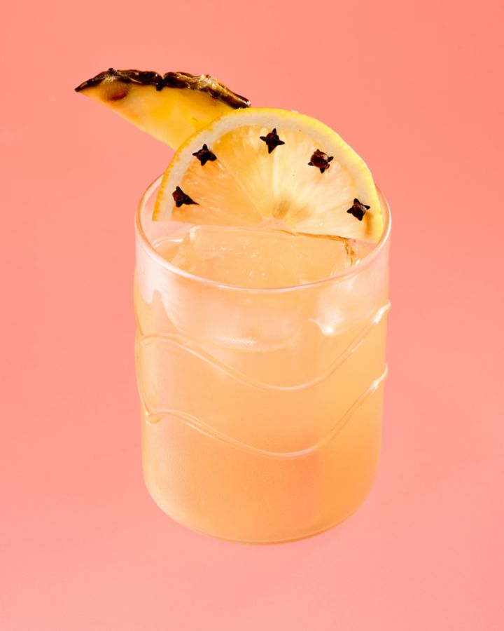 A glass of Pisco Punch, garnished with clove-studded lemon and pineapple
