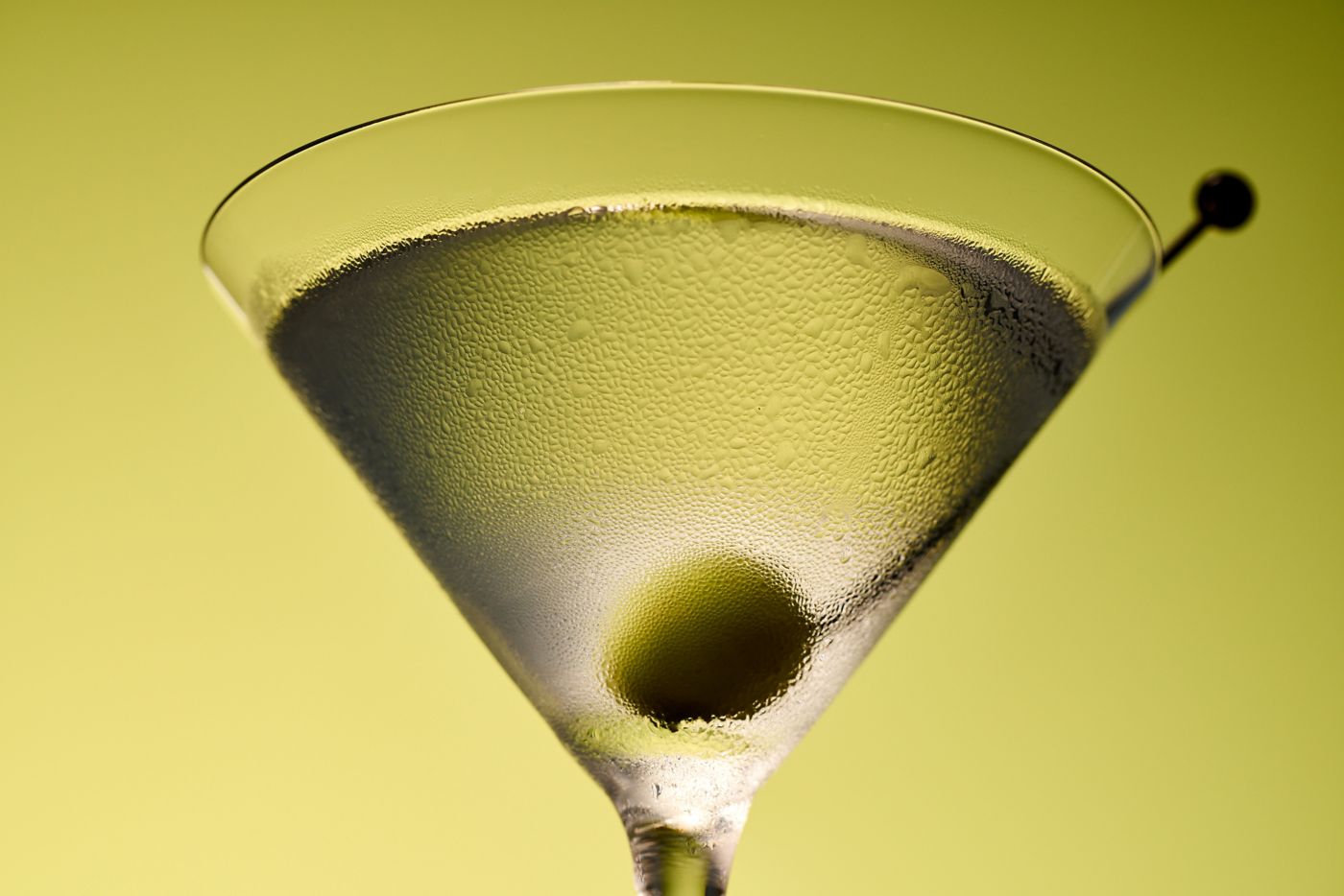 A close-up of a Martini with a skewered olive in it 