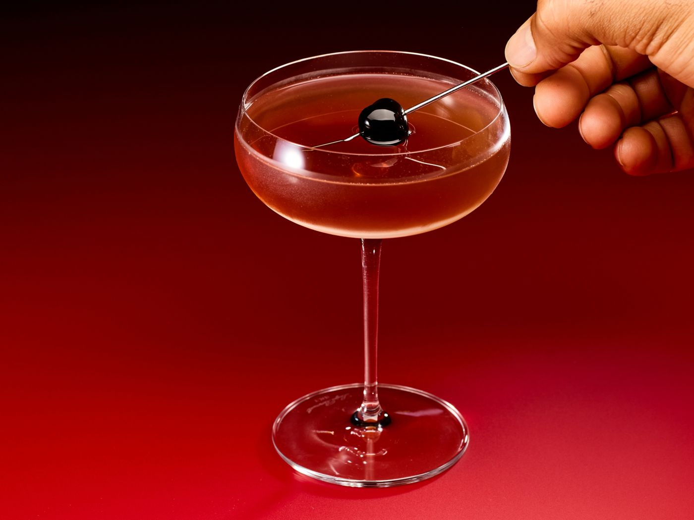 Placing a skewered cherry in a Manhattan cocktail 