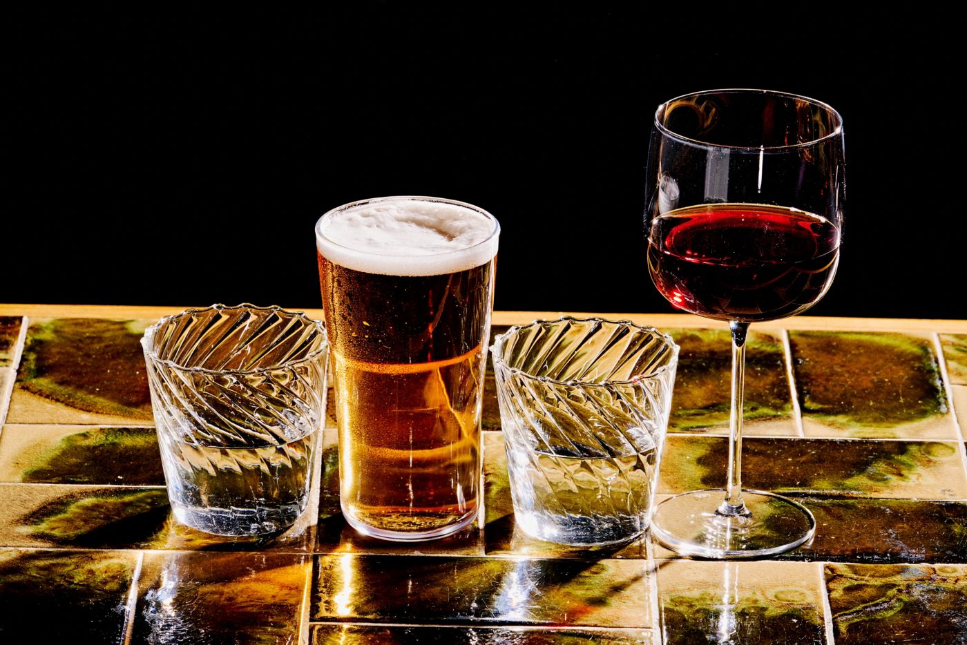 A beer and a glass of wine with waters next to them 