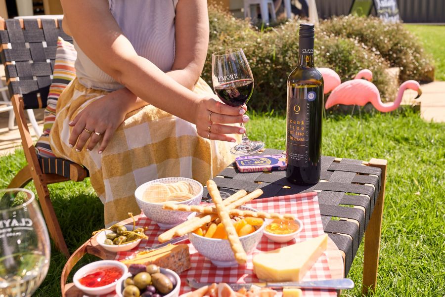 A lady sits at a picnic table outdoors holding a glass of red wine