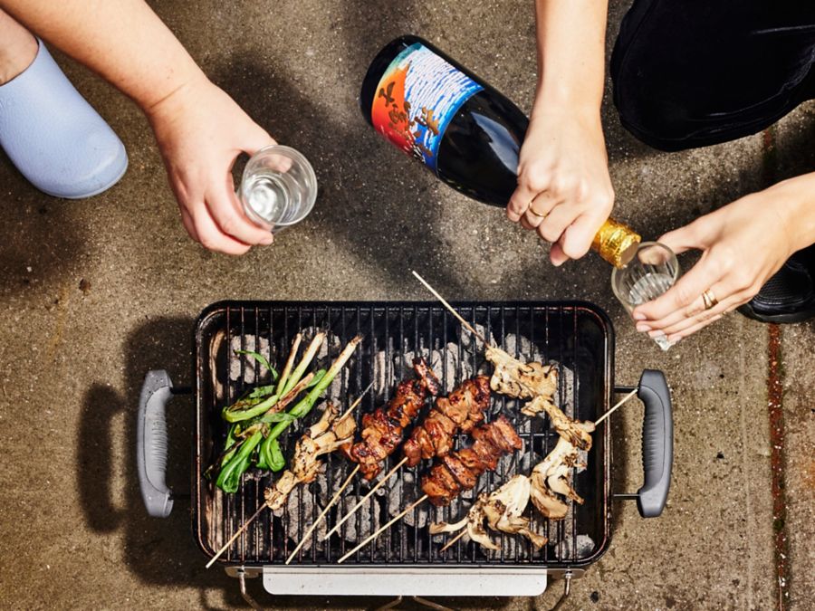 Yakitori cooking on a charcoal grill, with sake being poured. 