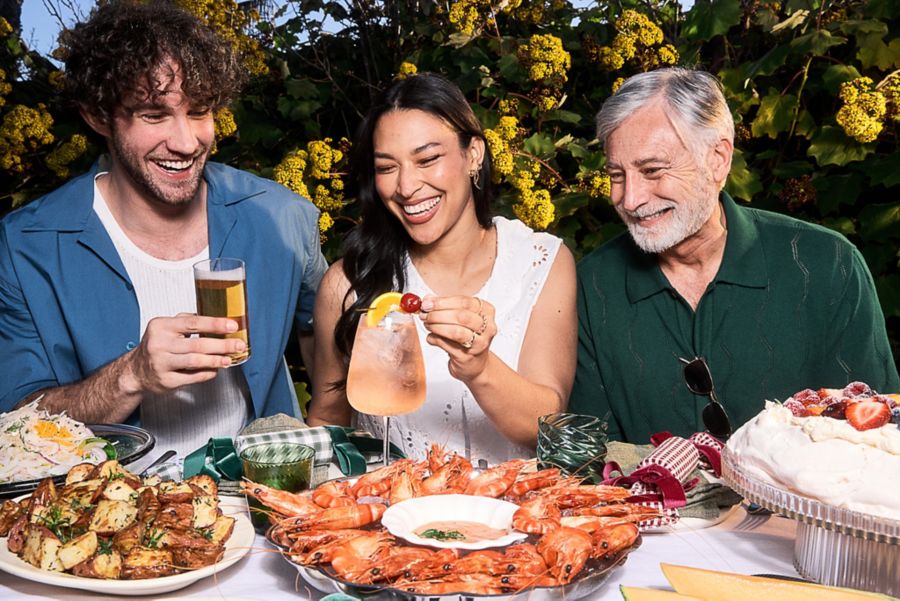 Young man, young woman and older man eating Christmas Day lunch of prawns and roast potatoes with cocktails