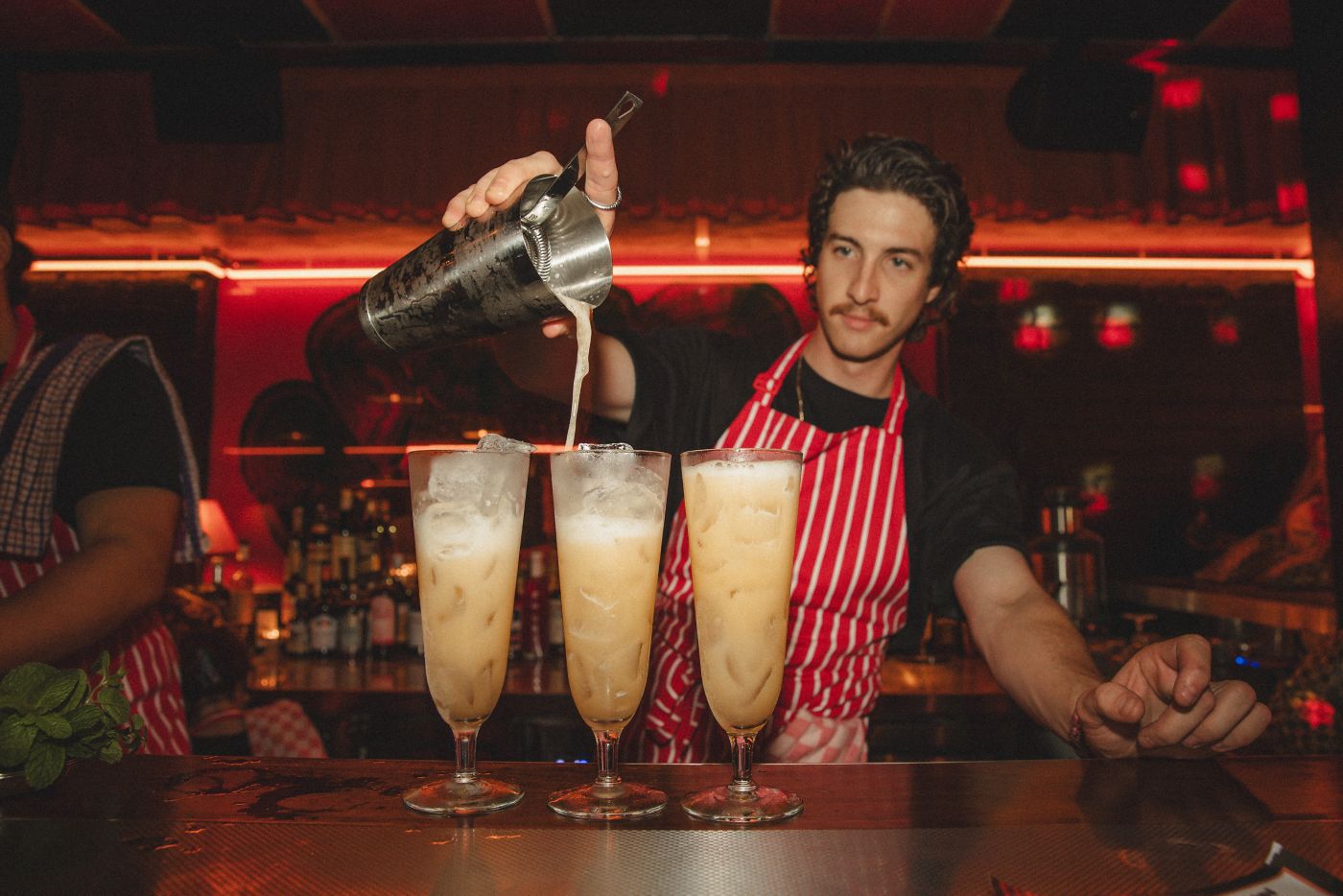 A bartender pouring out three cocktails at Herbs Taverne