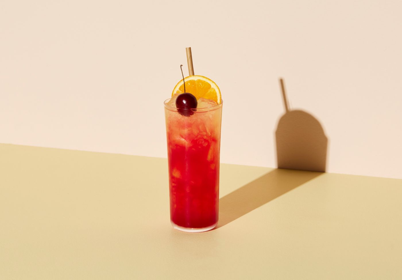 Tequila Sunrise cocktail in a tall glass with ice, orange wheel and fresh cherry garnish.