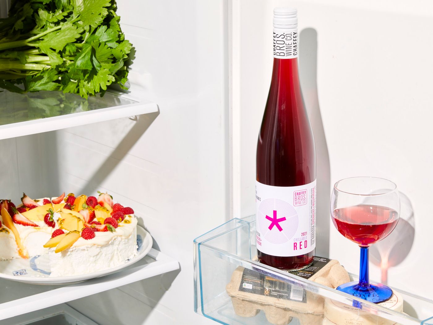 A chilled bottle of red wine with in a fridge door with a glass