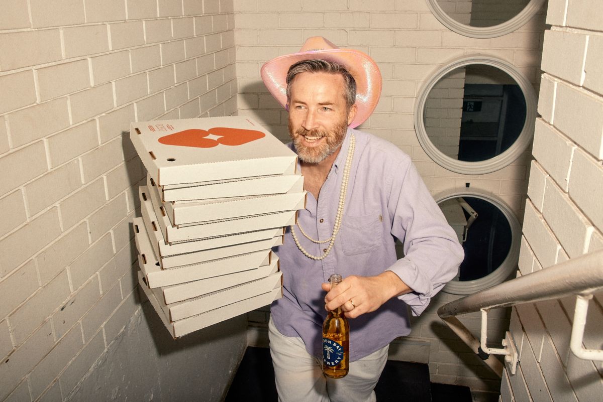 Stu carrying Byron Bay Brewery beer and pizza boxes up the stairs