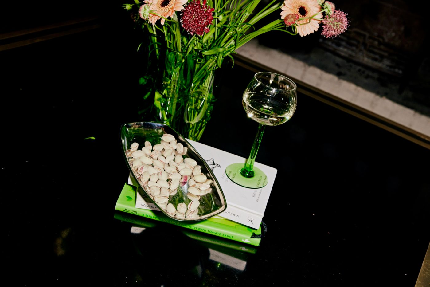A glass of white wine next to pistachios and a bunch of flowers