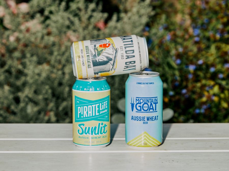 Three cans of wheat beer sitting on a bench outdoors