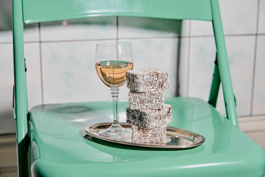 A plate of lamintons on a chair with a glass of sparkling moscato rosé