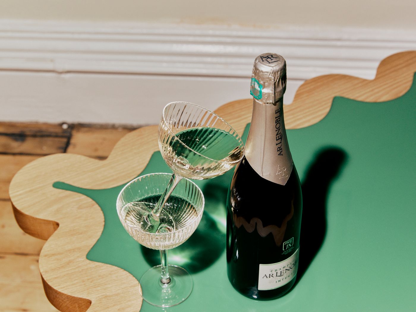 A bottle of Champagne and two coupe glasses next to it on a table