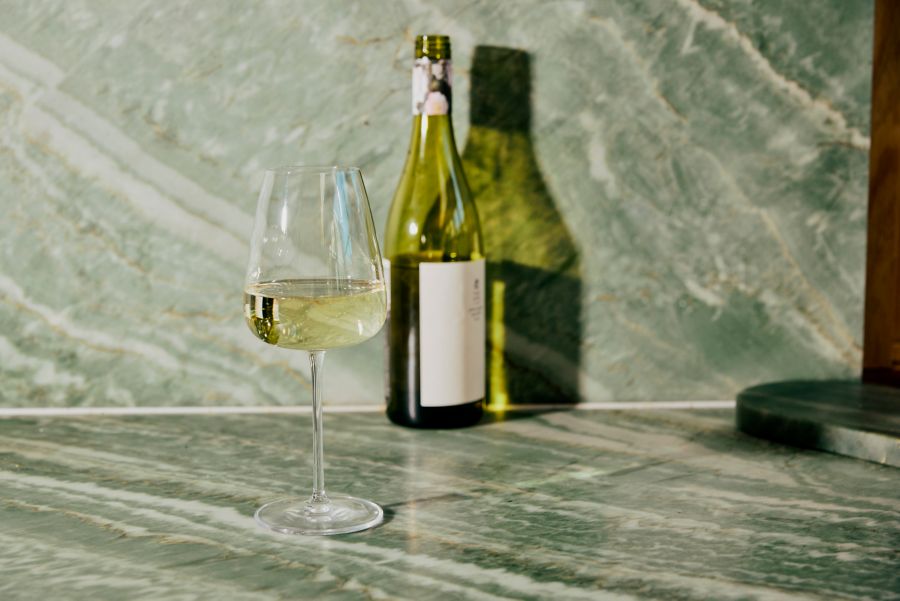 A bottle of pinot grigio with a glass of the wine in a green marble setting 