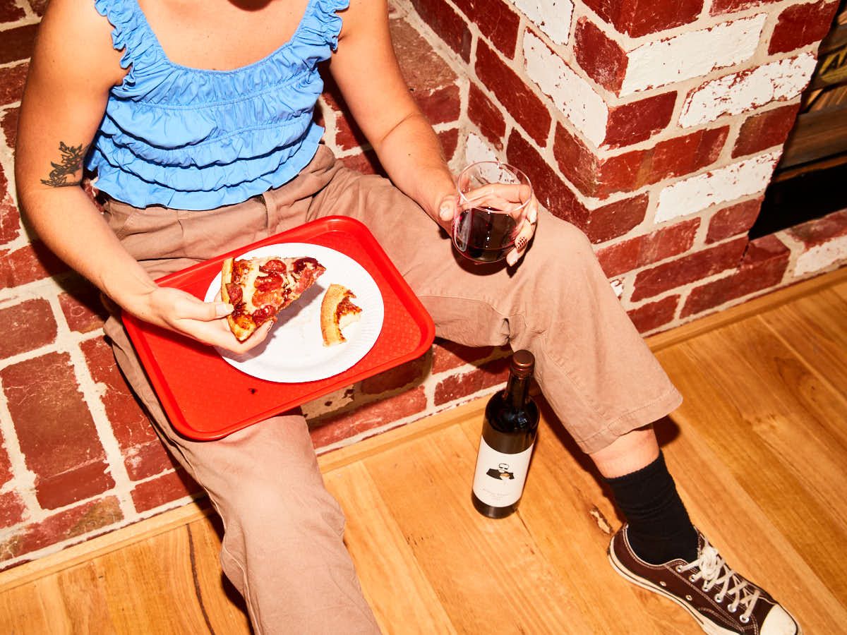 A person eating a slice of pizza with a glass of wine