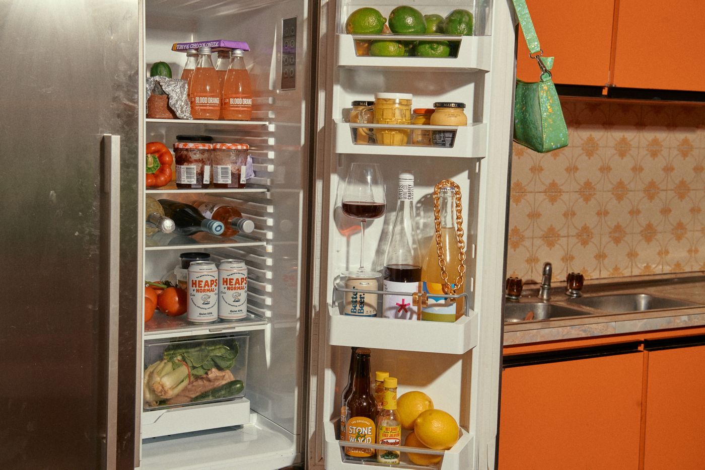 A kitchen with an open fridge holding various bottles of alcohol 