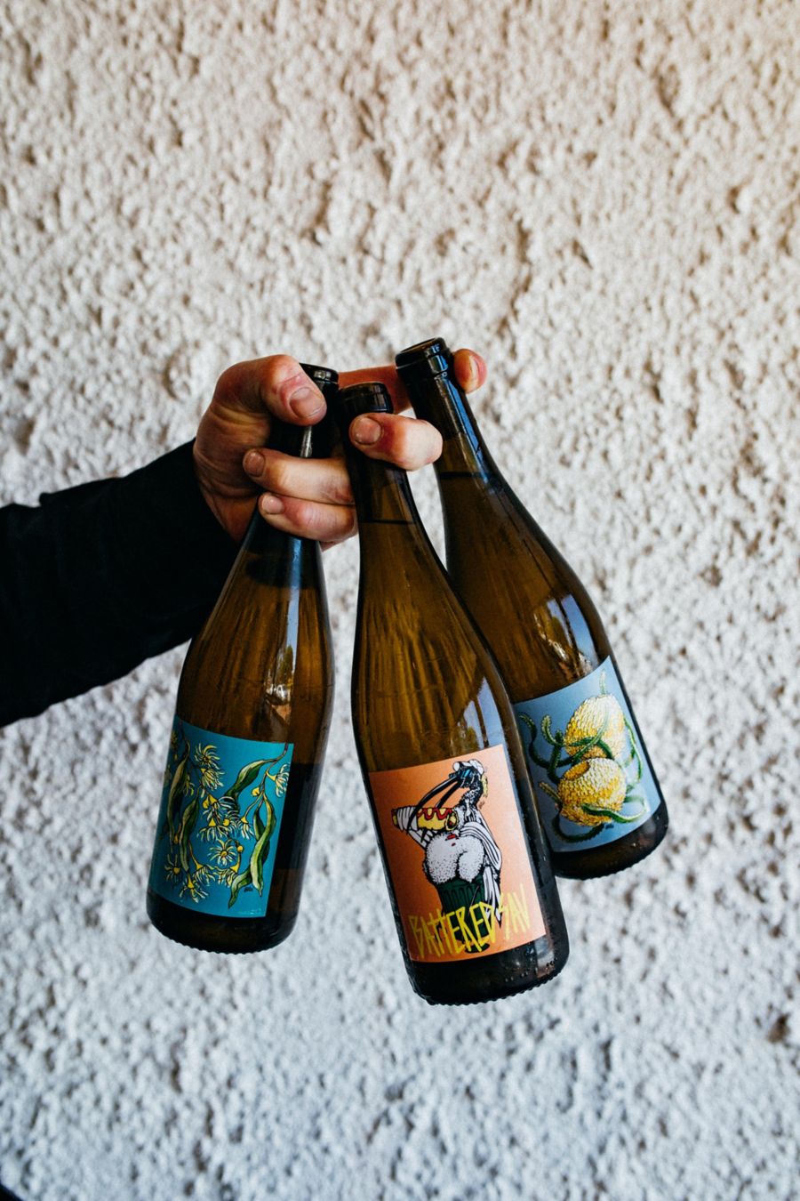 A hand holding three Beer bottle using his fingers