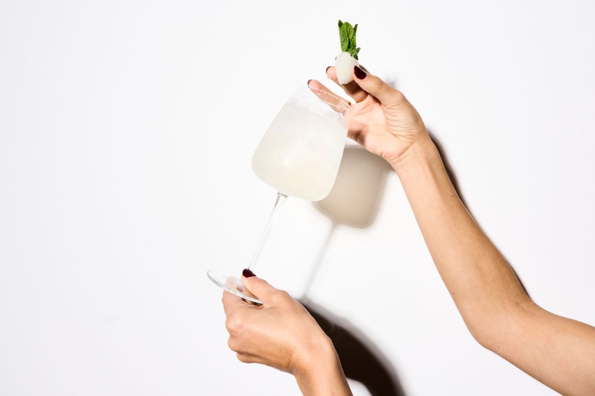 Holding the Lychee Spritz in a wine glass with lychee and mint for garnish  