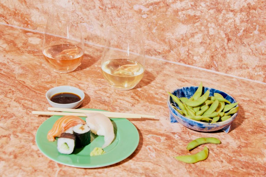 Two glasses of wine with a plate of sushi and edamame