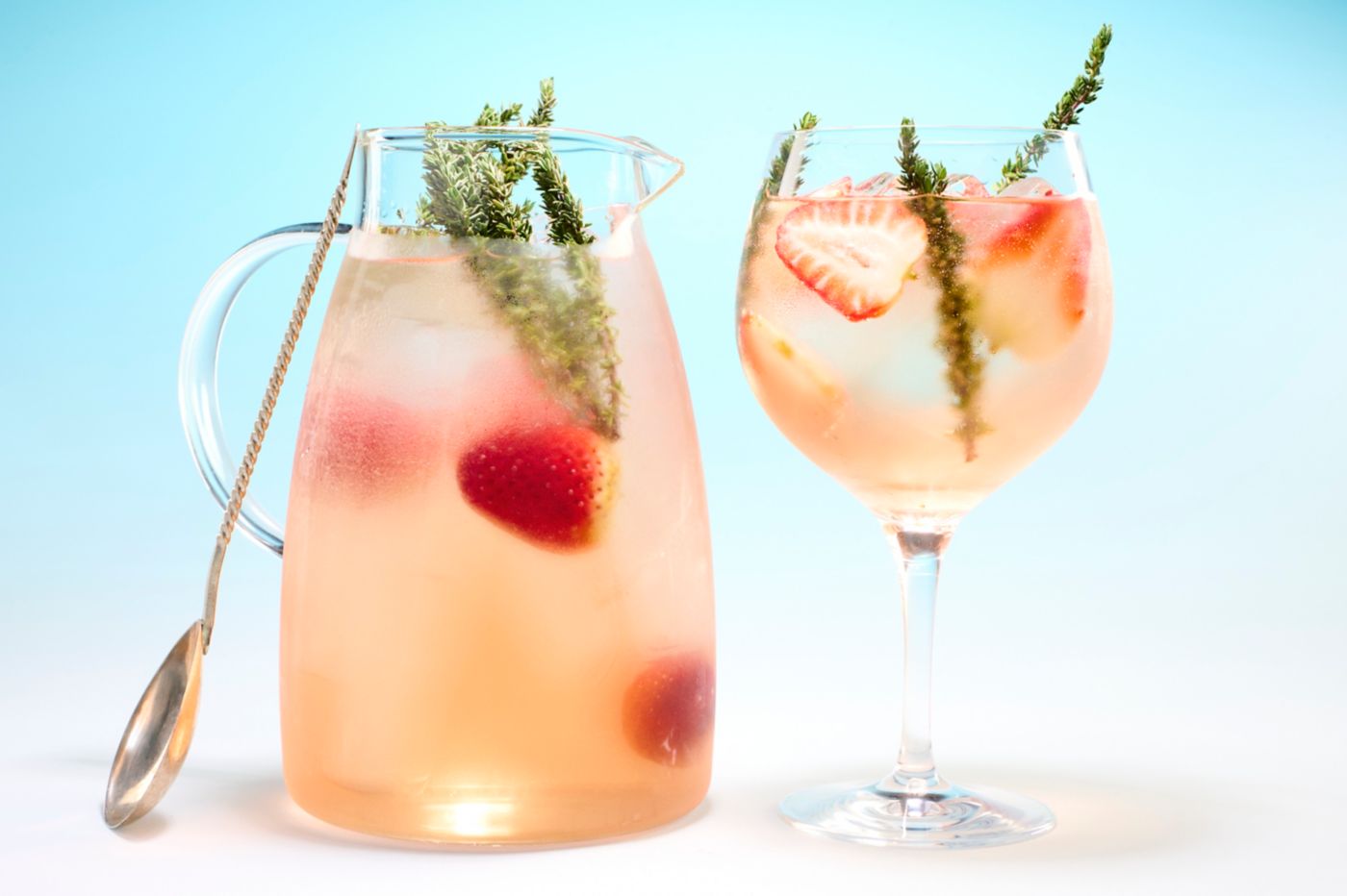 A jug and a glass of Rosé Spritzer with thyme and strawberries