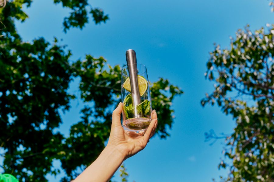 Holding up a tall glass with mint, lemon and a muddler against the sky