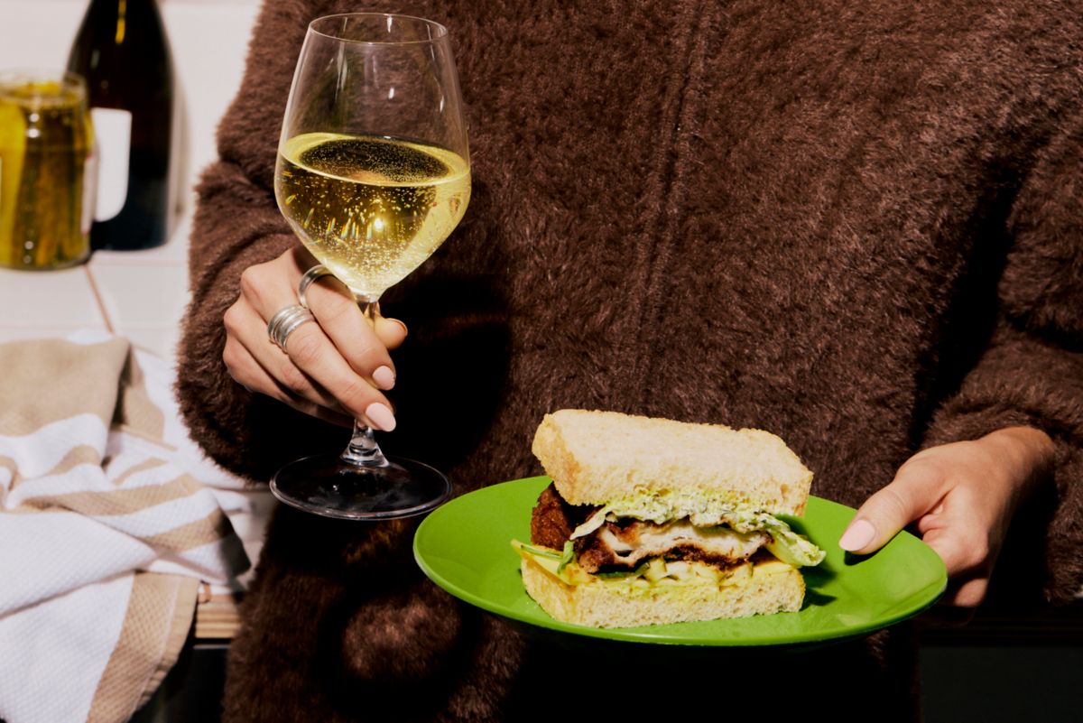 Holding a chicken sandwich and a glass of wine