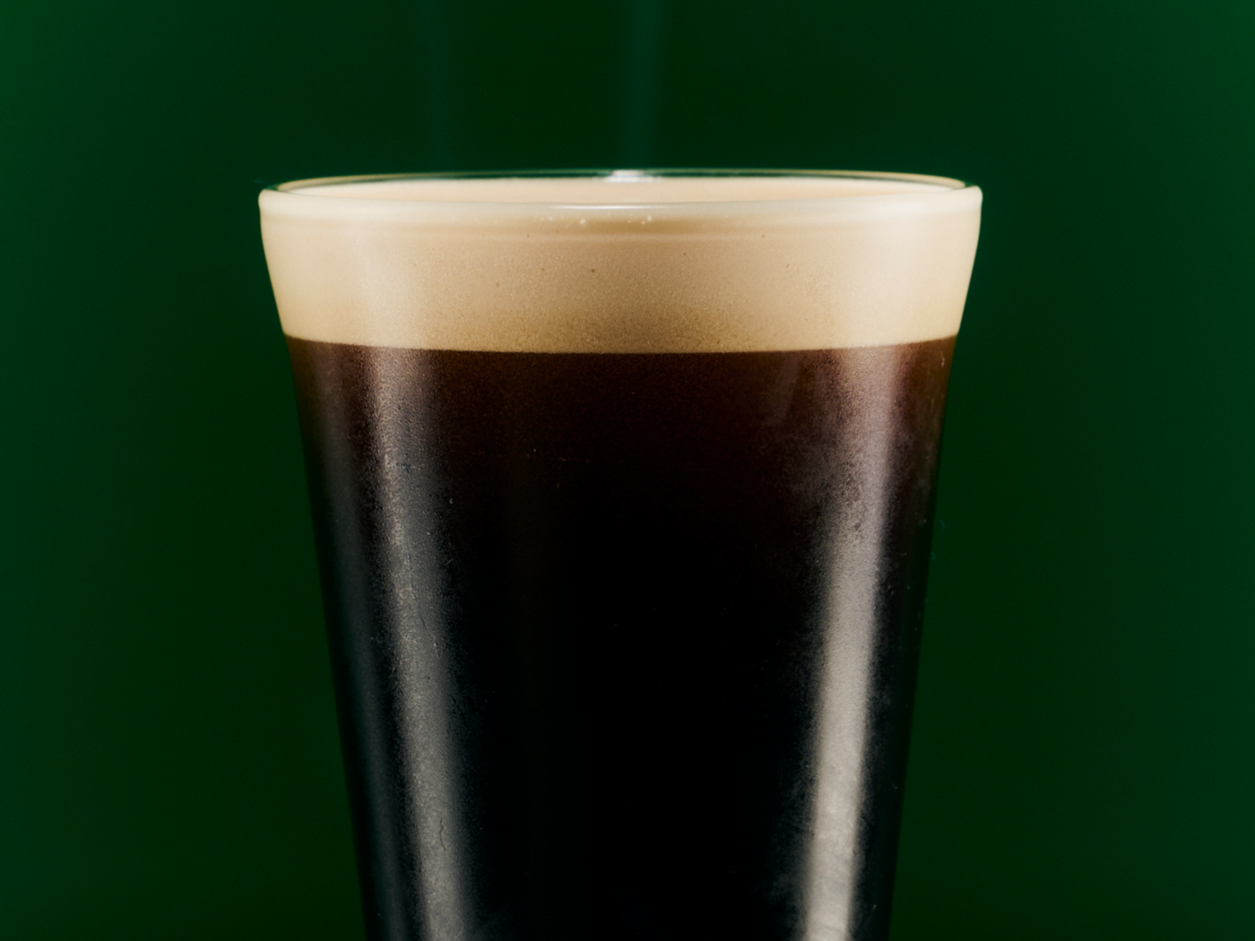 A cold glass of stout beer with a frothy head  