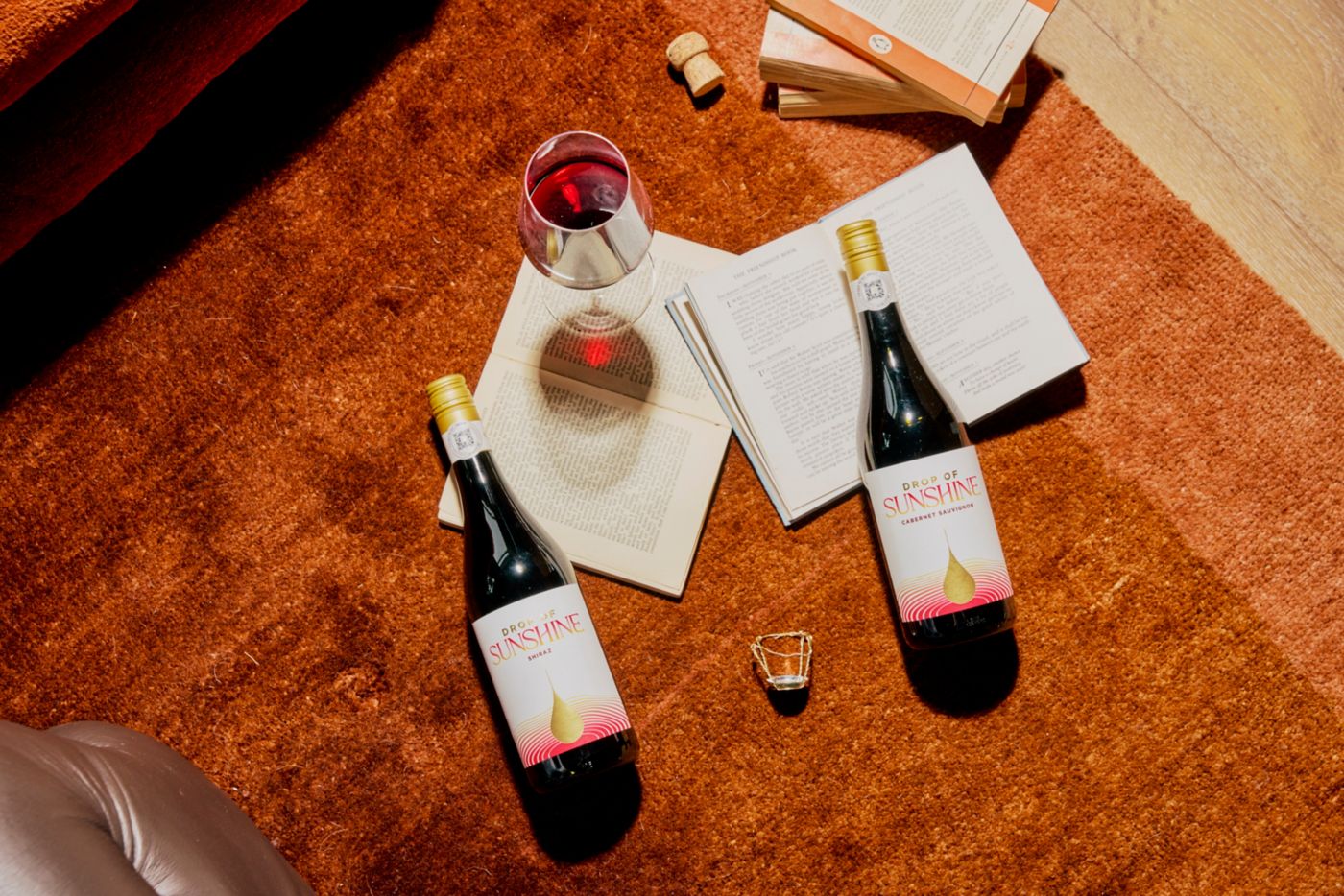 Two bottles of Drop of Sunshine with books and a glass of wine