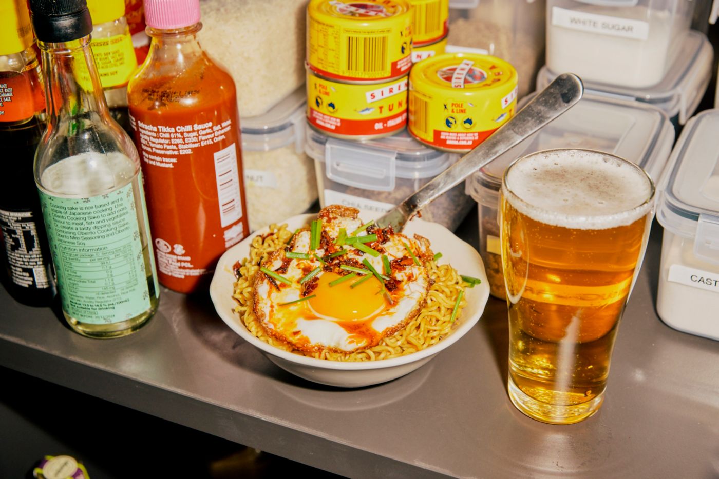 A bowl of Two Minute Noodles topped with a fried egg next to a glass of beer