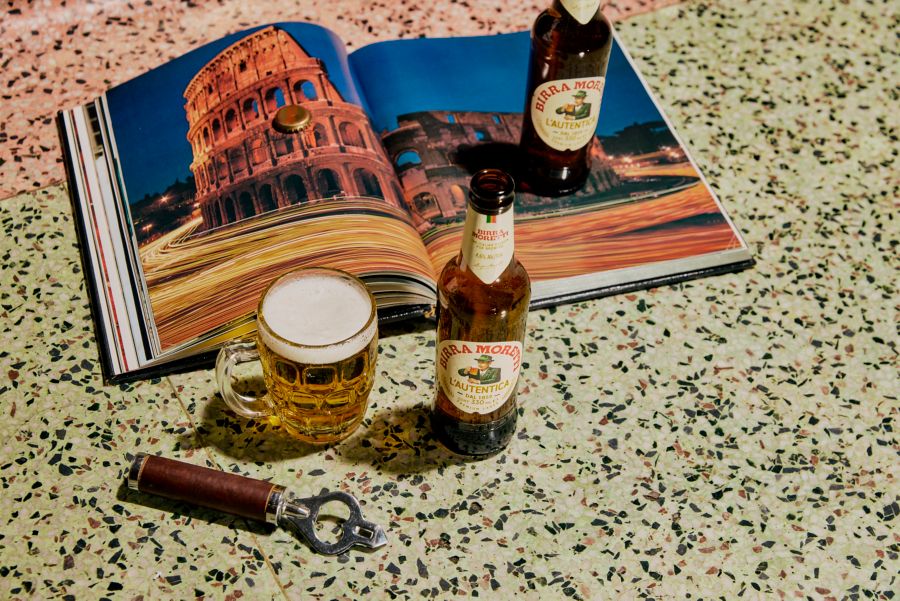 A glass and two bottles of Birra Moretti lager with a book on Italy