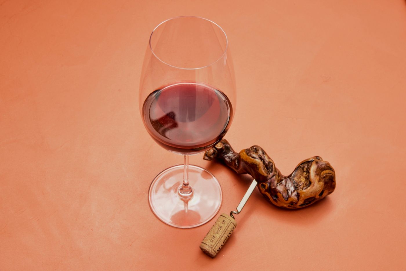 A glass of red wine with a corkscrew shaped like an old grapevine