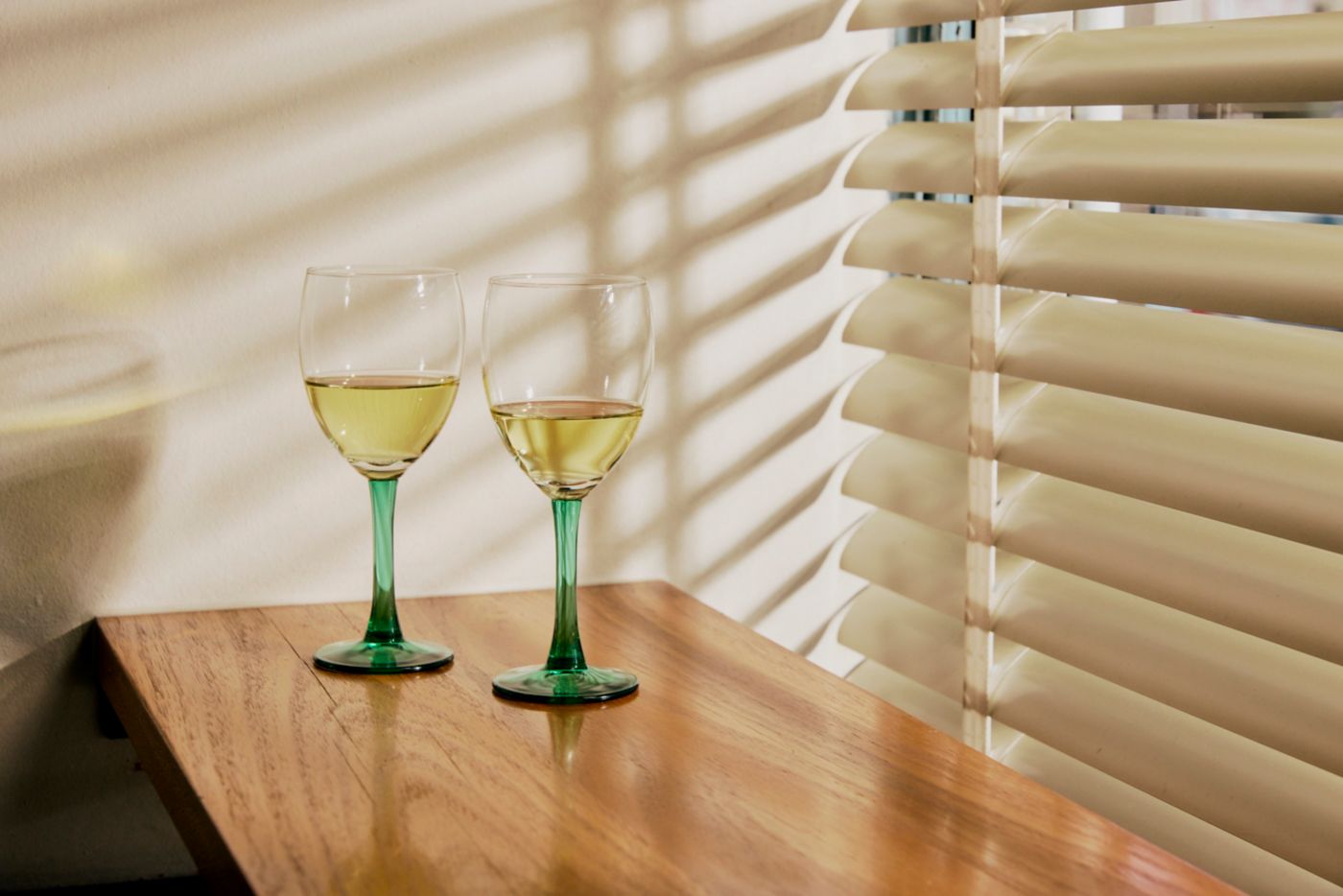 Two glasses of white wine on a bench next to a window