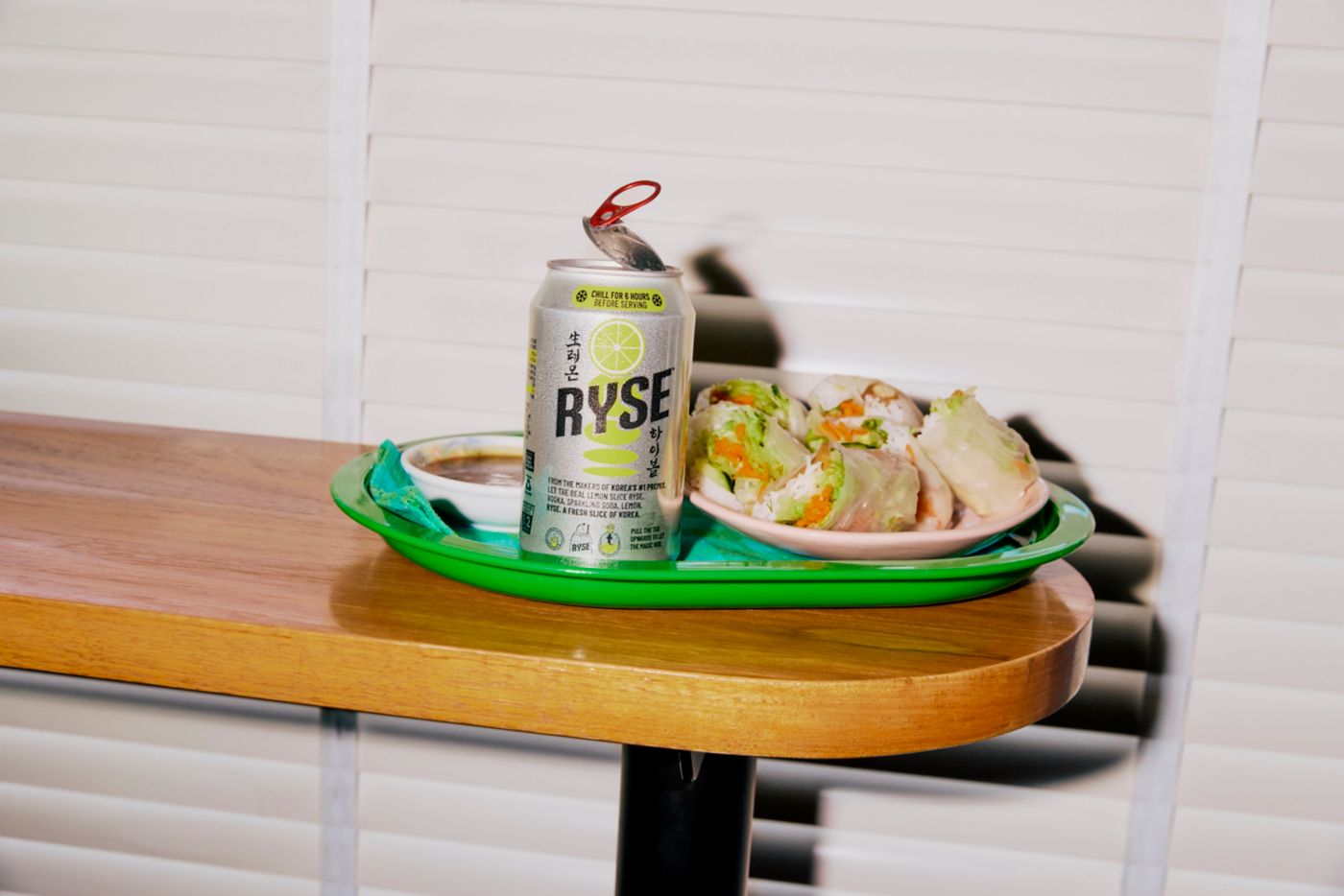 A plate of rice paper rolls on a table with a can of RYSE Vodka Lemon Soda