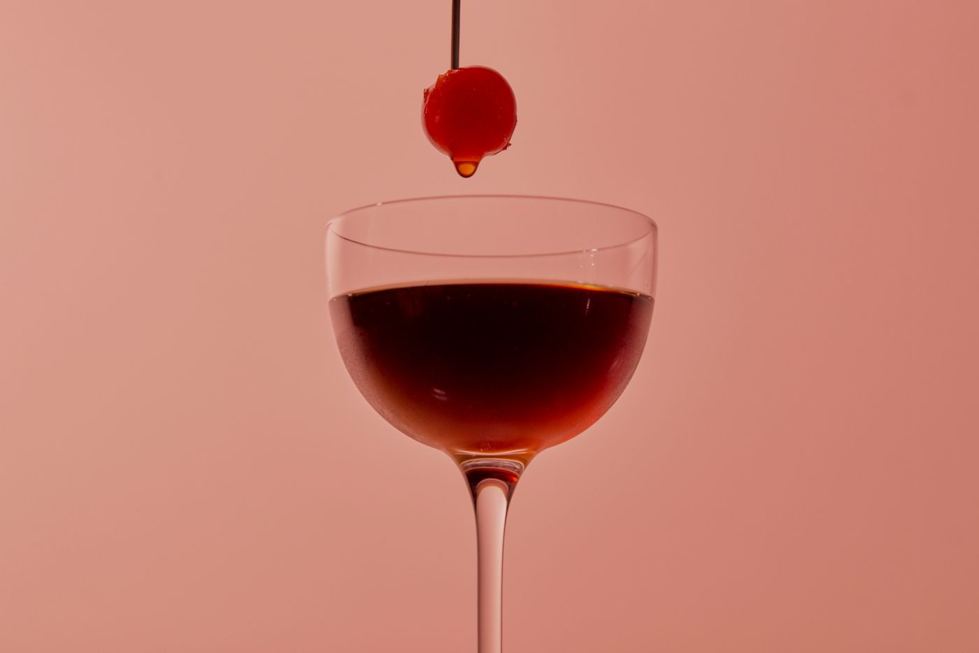 Holding a skewered cherry above the Black Manhattan