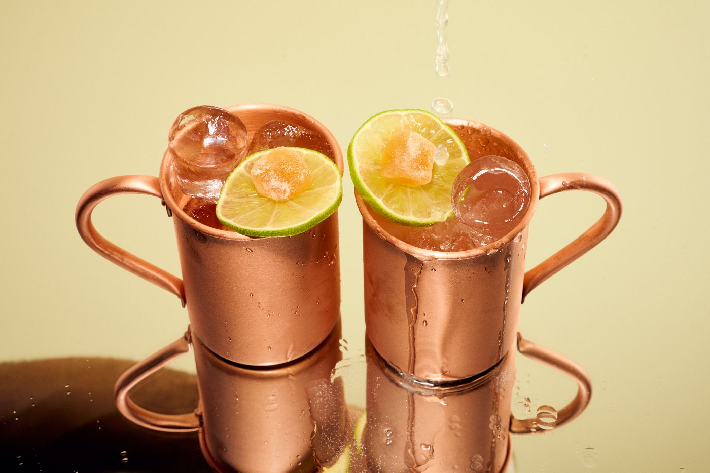 Two copper mugs of Moscow Mule cocktails, garnished with lime and ginger  