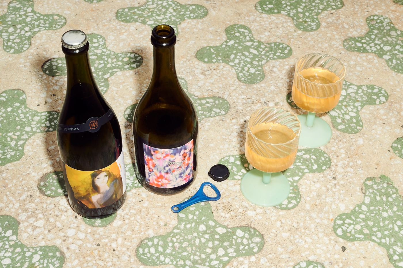 Two wine bottles with striking labels on a table with a glass of wine